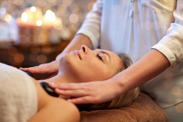 persone, bellezza, spa, stile di vita sano e concetto di relax - primo piano di una giovane e bella donna con massaggio con pietre calde nella spa