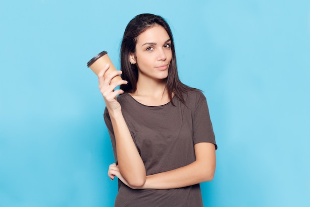 Persone, bevande e concetto di stile di vita - Giovane bella donna con caffè su sfondo blu. Donna attraente felice e sorridente. una donna con i capelli scuri tiene in mano un bicchiere di cartone con del caffè