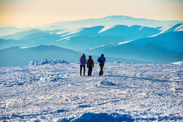 Persone che camminano al tramonto in inverno montagne coperte di neve