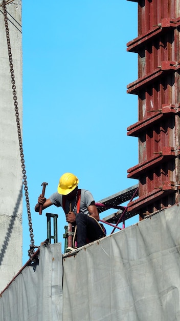 Persone che lavorano in cantiere con casco giallo e attrezzatura di sicurezza e che coprono l'edificio con vinile di colore grigio e cielo blu.