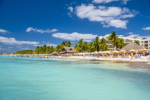 Persone che nuotano vicino alla spiaggia di sabbia bianca con ombrelloni bungalow bar e palme da cocco turchese Mar dei Caraibi Isla Mujeres isola Mar dei Caraibi Cancun Yucatan Messico