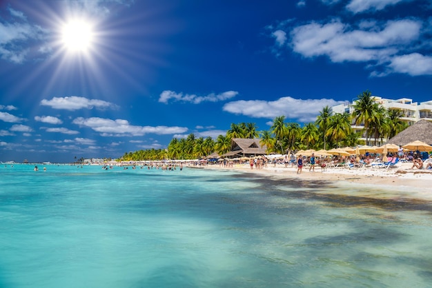 Persone che nuotano vicino alla spiaggia di sabbia bianca con ombrelloni bungalow bar e palme da cocco turchese Mar dei Caraibi Isla Mujeres isola Mar dei Caraibi Cancun Yucatan Messico