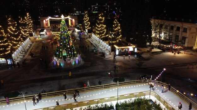 Persone che pattinano su una bellissima pista di pattinaggio su ghiaccio all'aperto decorate con illuminazioni natalizie di capodanno