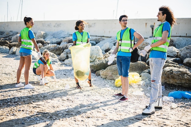 Persone che ripuliscono la spiaggia volontari che raccolgono i rifiuti sulla costa giovani amici della generazione z che lavorano in squadra consapevoli dell'inquinamento prodotto dall'industria della plastica