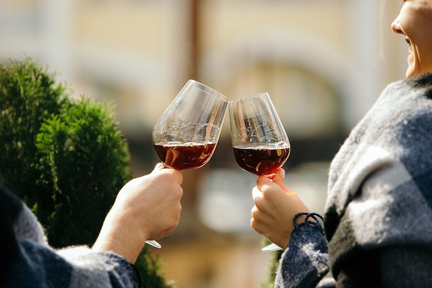 Persone che tintinnano bicchieri di vino sulla terrazza estiva del bar o del ristorante. Amici allegri felici celebrano la festa estiva o autunnale. Immagine ravvicinata di mani umane, stile di vita.