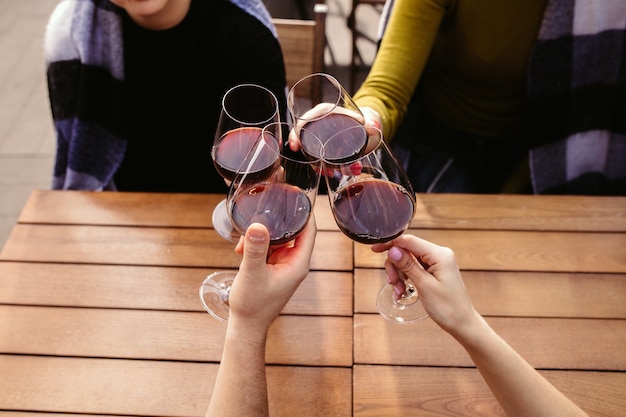 Persone che tintinnano bicchieri di vino sulla terrazza estiva del bar o del ristorante. Amici allegri felici celebrano la festa estiva o autunnale. Immagine ravvicinata di mani umane, stile di vita.