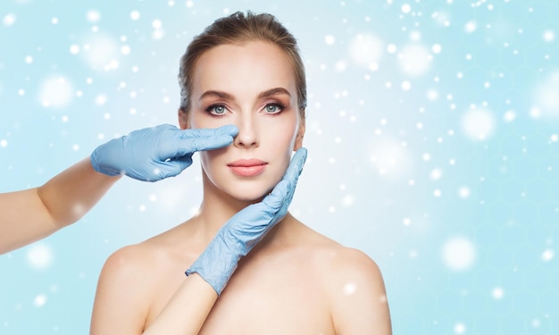 persone, cosmetologia, chirurgia plastica e concetto di bellezza - mani di chirurgo o estetista che toccano il viso della donna su sfondo blu e neve