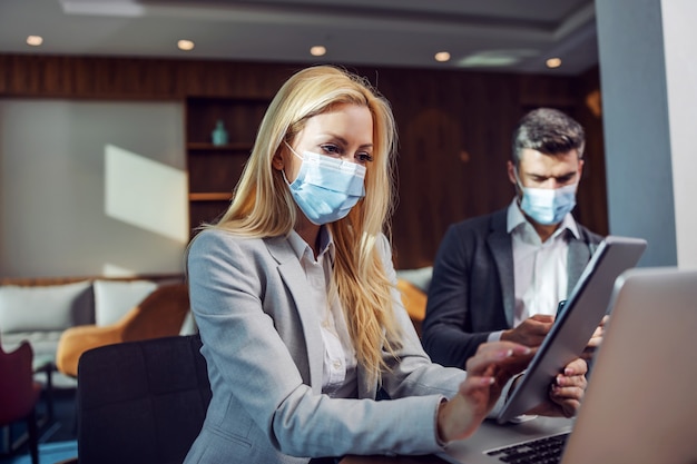 Persone di affari con maschere facciali seduti in un caffè e avendo riunioni di lavoro. Donna che utilizza una tavoletta. Zoom meeting, tecnologia, telecomunicazioni durante COVID-19, coronavirus