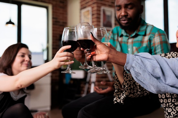 Persone diverse sorridenti felici che tintinnano i bicchieri mentre celebrano l'evento di compleanno. Gioioso gruppo multirazziale di migliori amici che brindano a bicchieri di vino mentre si godono la festa del vino a casa.