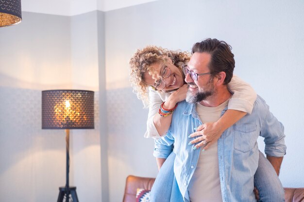 Persone e felice tempo libero concetto indoor persone felici coppia uomo e donna in piggyback divertirsi e godersi insieme la casa sorridendo e ridendo molto adulto acquisto piatto e festeggiare felicissimo