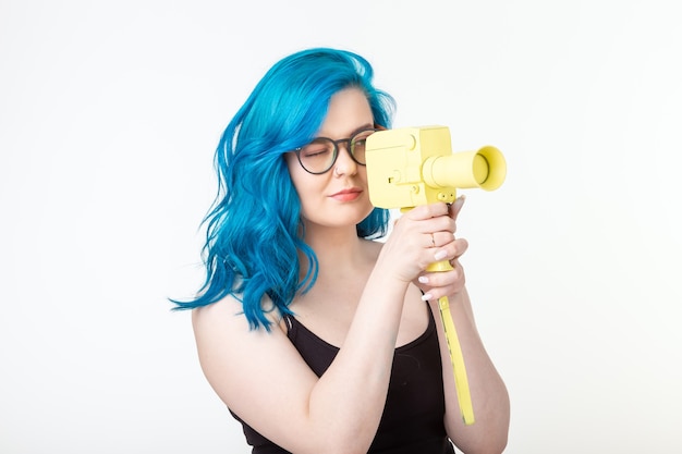 Persone, hobby e concetto di moda - La bella ragazza con i capelli blu tiene la retro macchina fotografica gialla sulla parete bianca