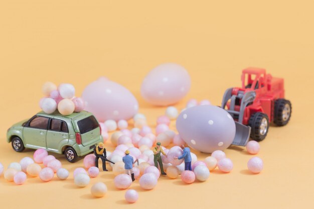 Persone (in miniatura) che preparano le vacanze di Pasqua del distributore automatico di giocattoli Egg. Composizione di messa a fuoco selettiva e morbido colore pastello tonico