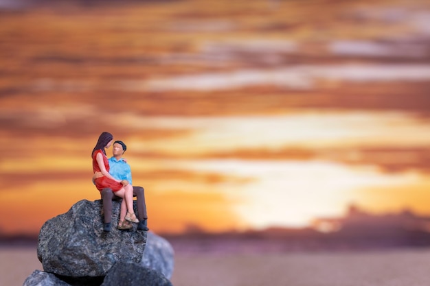 Persone in miniatura Coppia seduta su una spiaggia del mare con sfondo del tramonto