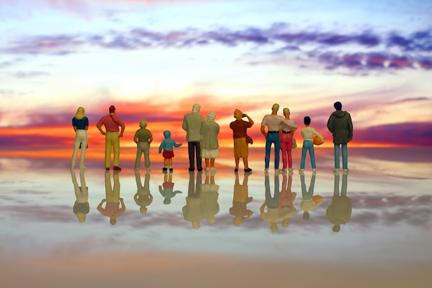 Persone in miniatura di diverse età che guardano il tramonto sulla spiaggia