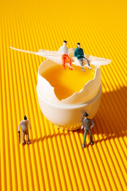 Persone in miniatura e uova su sfondo giallo testurizzato
