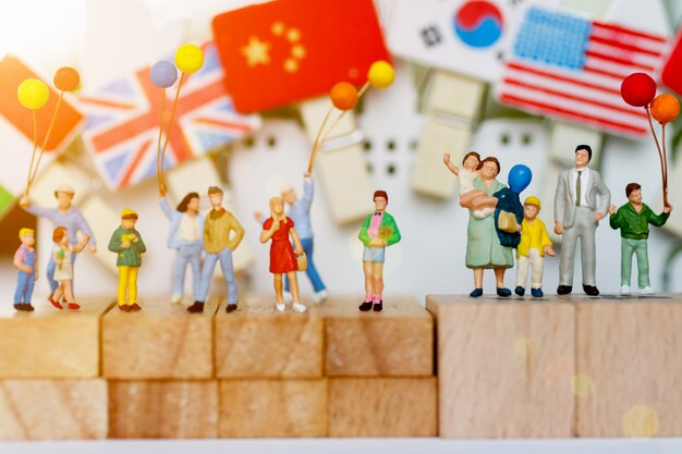 Persone in miniatura, famiglia e bambini con palloncini colorati in piedi sul blocco di legno.