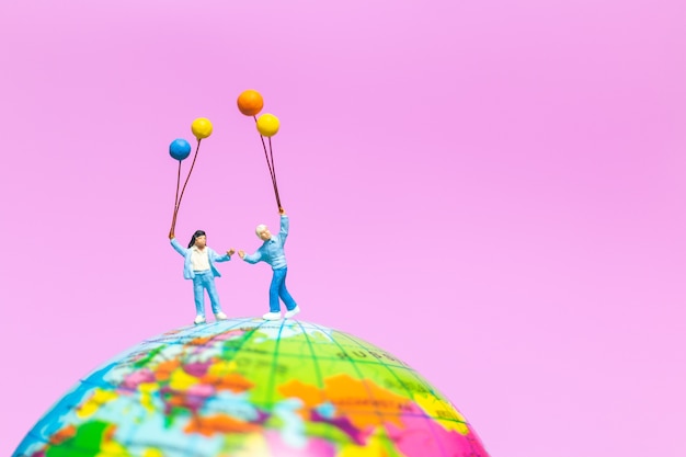 Persone in miniatura: famiglia felice azienda palloncino sul globo con sfondo rosa