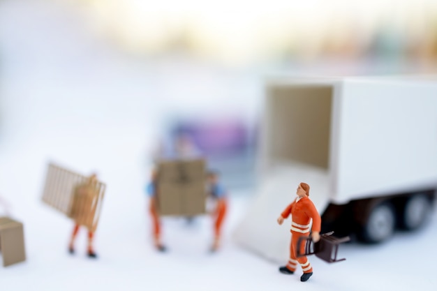 Persone in miniatura: scatola di caricamento del lavoratore e monete per il contenitore del camion. Concetto di servizio di spedizione e consegna online.