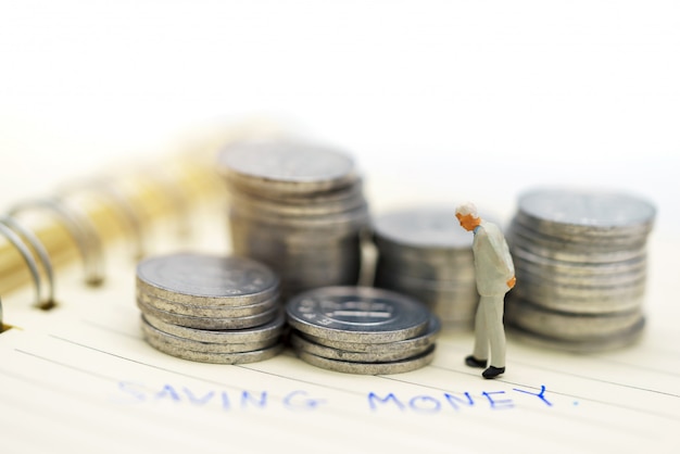 Persone in miniatura: uomini d'affari in piedi con la pila di monete, finanza e concetto di investimento.