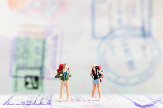 Persone in miniatura: viaggiatore con zaino che cammina sul passaporto