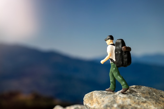 Persone in miniatura: Viaggiatore con zaino che cammina sulla roccia, concetti di viaggio e avventura.