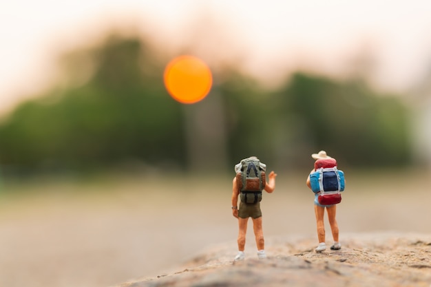 Persone in miniatura: viaggiatore con zaino che cammina sulla roccia