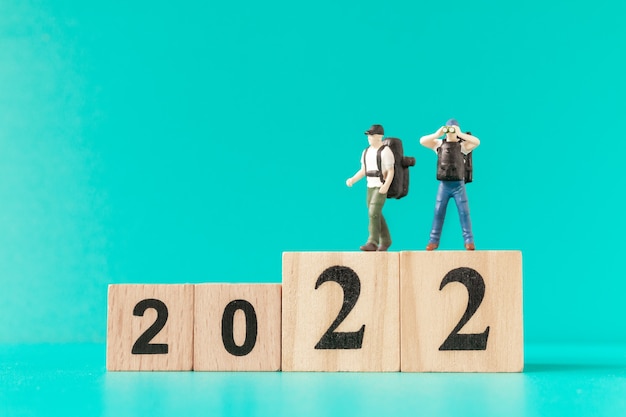 Persone in miniatura: zaino in spalla e turista in piedi sul blocco di legno numero 2022, concetto di felice anno nuovo