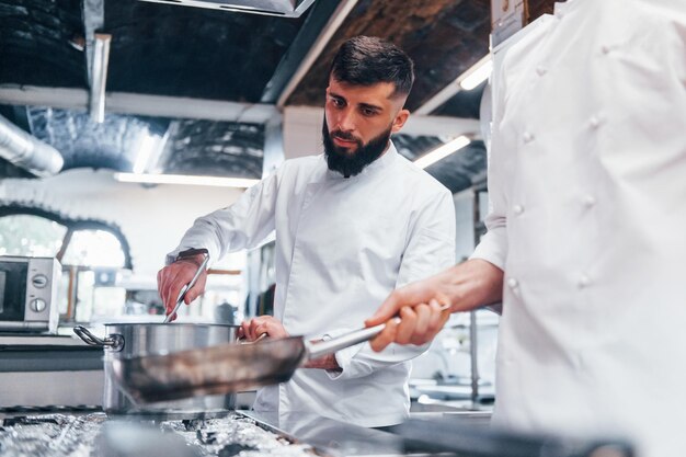 Persone in uniforme bianca che cucinano insieme il cibo in cucina Giornata intensa al lavoro