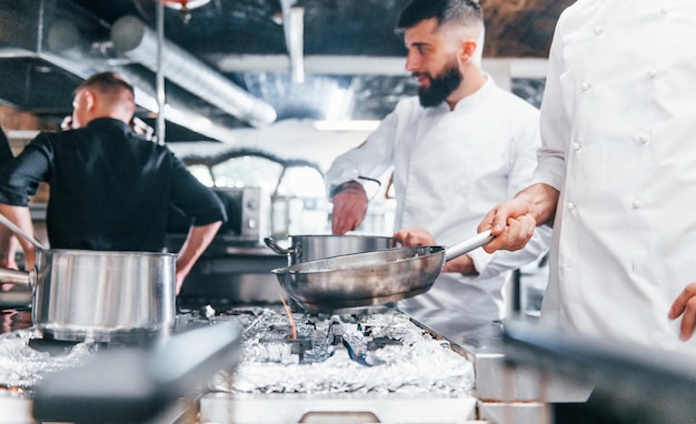 Persone in uniforme bianca che cucinano insieme il cibo in cucina Giornata intensa al lavoro