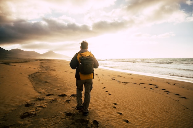 Persone in vista posteriore che camminano da sole con il suo zaino sulla desolazione bellissima spiaggia selvaggia per un concetto alternativo di turismo vacanza avventura ed esplorare la libertà del luogo panoramico e sentire la natura