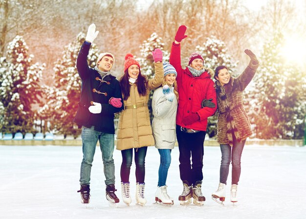 persone, inverno, amicizia, sport e tempo libero concetto - amici felici pattinaggio su ghiaccio e agitare le mani sulla pista all'aperto