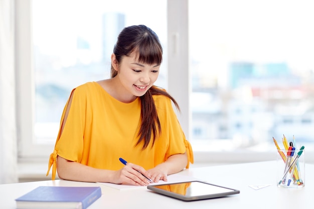 persone, istruzione, scuola superiore e concetto di apprendimento - felice giovane studentessa asiatica con computer tablet pc, libro e blocco note che scrivono a casa