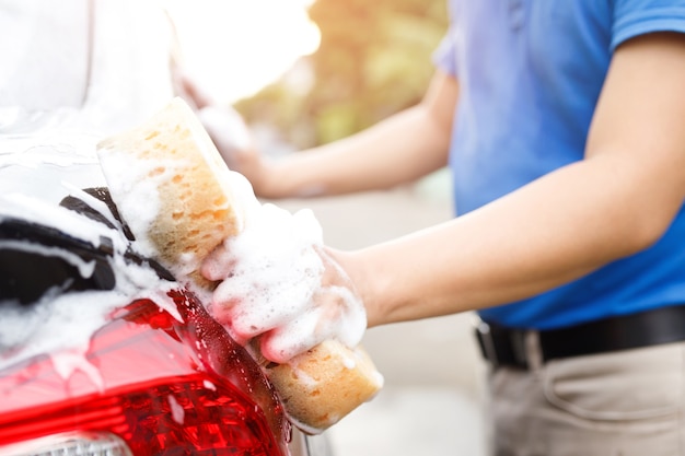 Persone lavoratore uomo che tiene la mano spugna gialla e finestra detergente schiuma a bolle per il lavaggio auto. Concetto di autolavaggio pulito. Lascia spazio per scrivere messaggi.