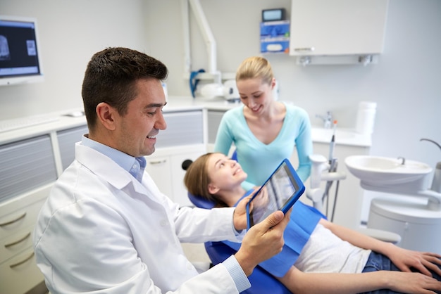 persone, medicina, stomatologia, tecnologia e concetto di assistenza sanitaria - dentista maschio felice che guarda i raggi x dei denti sul computer tablet pc e ragazza paziente con sua madre presso l'ufficio della clinica odontoiatrica