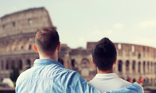 persone, omosessualità, matrimonio omosessuale, concetto di viaggio e amore - primo piano di coppia gay maschio felice che si abbraccia dal retro sul Colosseo sullo sfondo di roma