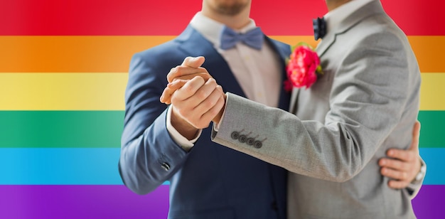 persone, omosessualità, matrimonio omosessuale e concetto di amore - primo piano di coppia gay maschio felice che si tiene per mano e balla sul matrimonio su sfondo bandiera arcobaleno