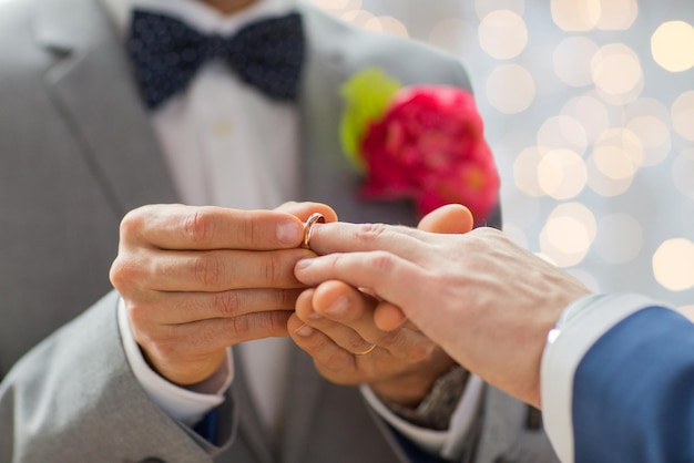 persone, omosessualità, matrimonio omosessuale e concetto di amore - primo piano di coppie gay maschi felici che mettono l'anello nuziale su sfondo di luci