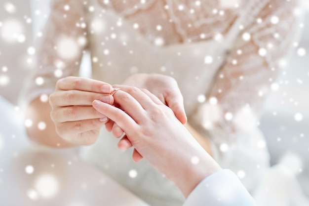 persone, omosessualità, matrimonio tra persone dello stesso sesso e concetto di amore - primo piano delle mani di una coppia lesbica felice che indossa l'anello nuziale sopra l'effetto neve