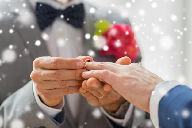 persone, omosessualità, matrimonio tra persone dello stesso sesso e concetto di amore - primo piano di felici coppie gay maschili che mettono l'anello nuziale sopra l'effetto neve