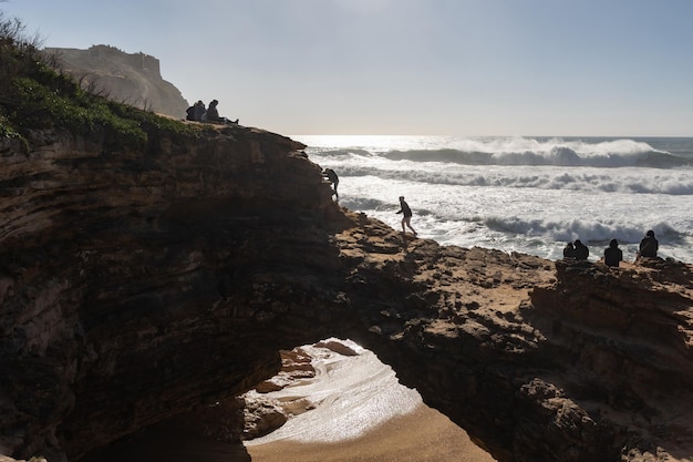 Persone sedute e che camminano sulle rocce e guardano le onde del mare