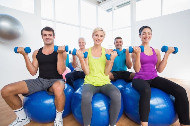 Persone sedute su palle e sollevamento pesi in palestra