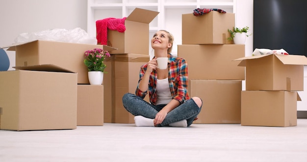 persone, spostamento di un nuovo posto e concetto di riparazione bella giovane donna felice con molte scatole di cartone sedute sul pavimento con la tazza a casa