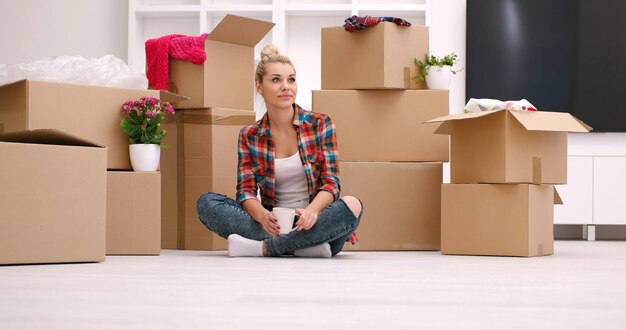 persone, spostamento di un nuovo posto e concetto di riparazione bella giovane donna felice con molte scatole di cartone sedute sul pavimento con la tazza a casa
