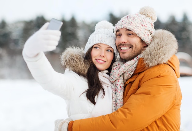 Persone, stagione, amore, tecnologia e concetto di svago - coppia felice che si fa selfie con lo smartphone su sfondo invernale