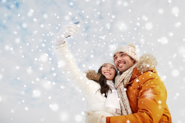 Persone, stagione, amore, tecnologia e concetto di svago - coppia felice che si fa selfie con lo smartphone su sfondo invernale