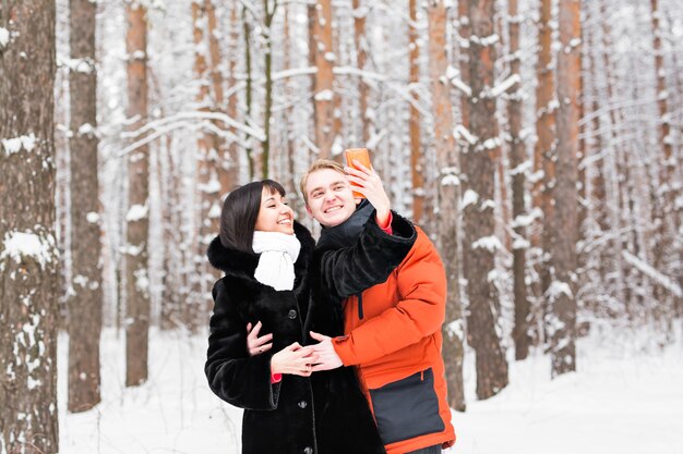 Persone, stagione, amore, tecnologia e concetto di tempo libero - coppia felice che scatta foto con il bastone selfie dello smartphone su sfondo invernale