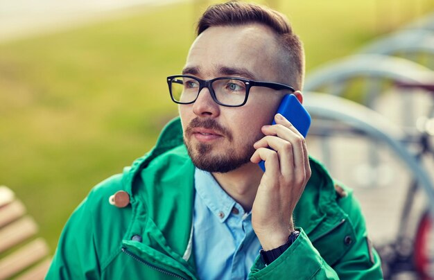 persone, stile, tecnologia e stile di vita - giovane hipster che chiama smartphone e si siede su una panchina in città