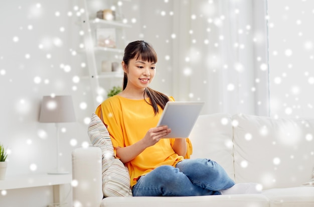 persone, tecnologia e tempo libero concetto - felice giovane donna asiatica seduta sul divano con tablet computer a casa sopra la neve