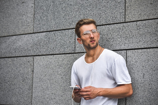 Persone, tecnologia, viaggi e turismo - uomo con auricolari, smartphone sulla strada della città e ascolto di musica su sfondo grigio muro