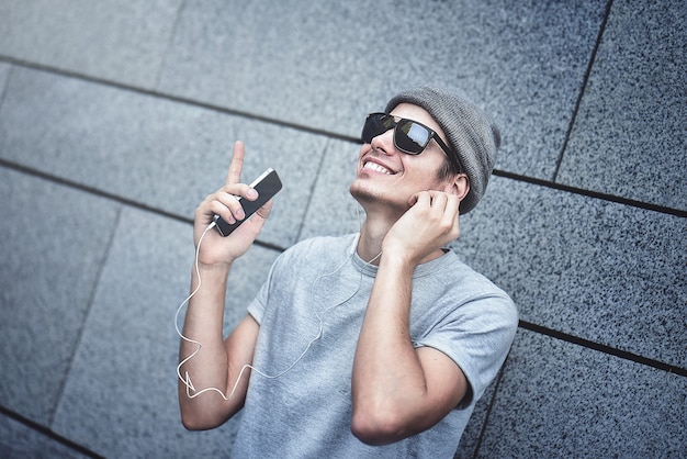 Persone, tecnologia, viaggi e turismo - uomo con auricolari, smartphone sulla strada della città e ascolto di musica su sfondo grigio muro